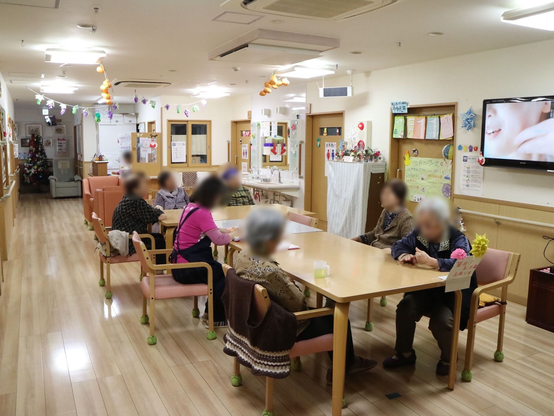 空調設備が何台も設置されている共有スペースである。椅子、テーブルなどが並べられており、スタッフや入居者様たちが座っている。