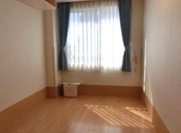 壁に緊急通報装置を設置したフローリングの部屋。大きな窓にはカーテンが付き、家具は置かれていない。