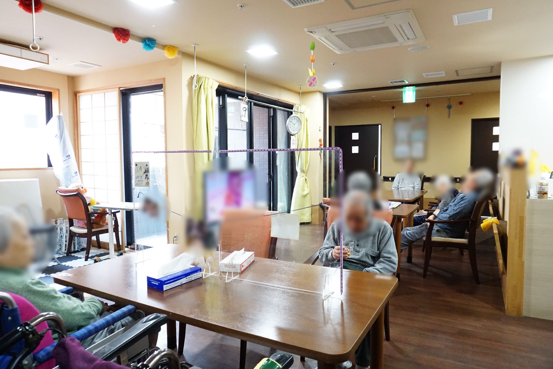 ブルーのエプロンを付けた女性スタッフが車いすの高齢女性に寄り添い、女性はどこかを指さしている。