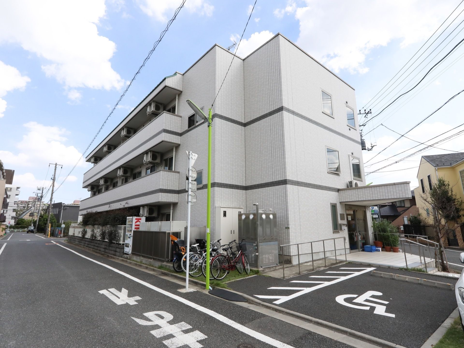 施設は白色の外壁で、３階建ての建物となっている。玄関のそばには、駐車スペースや駐輪場も設けられている。