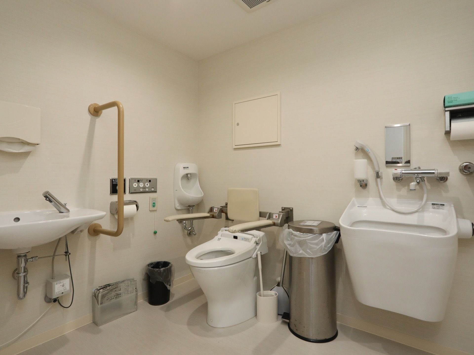 清潔感のあるトイレに洗面台、温水洗浄便座、シャワー口が付いたスロップシンクが設置されている。壁には手すりがある。