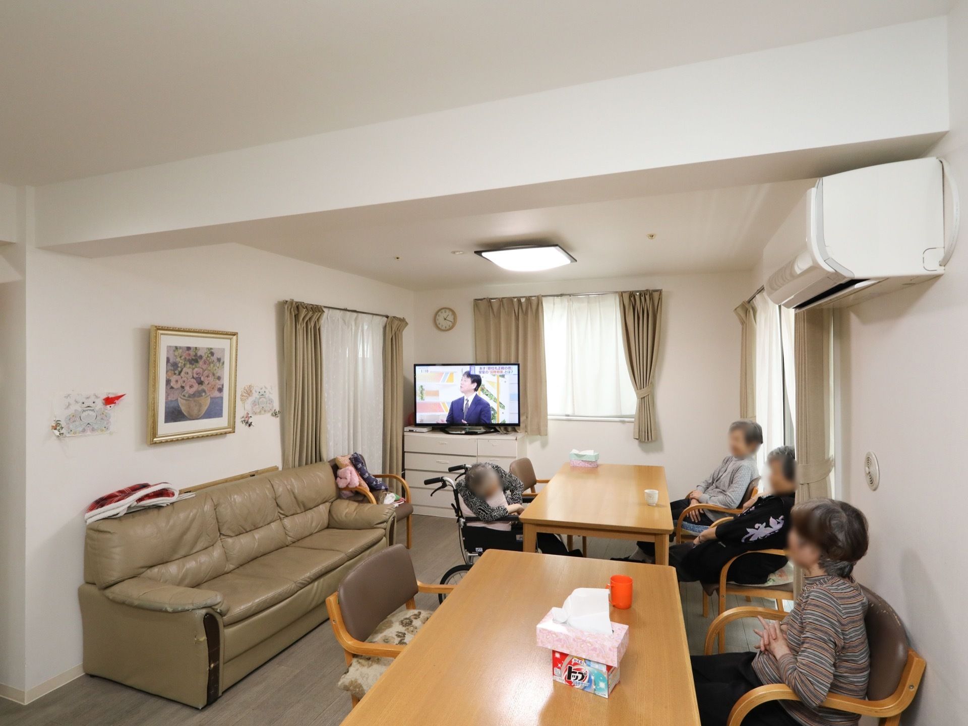 共有スペースのダイニングテーブルのところに入居者様が座り、テレビ鑑賞をしたり、うたた寝をしたり、自由に過ごしている。