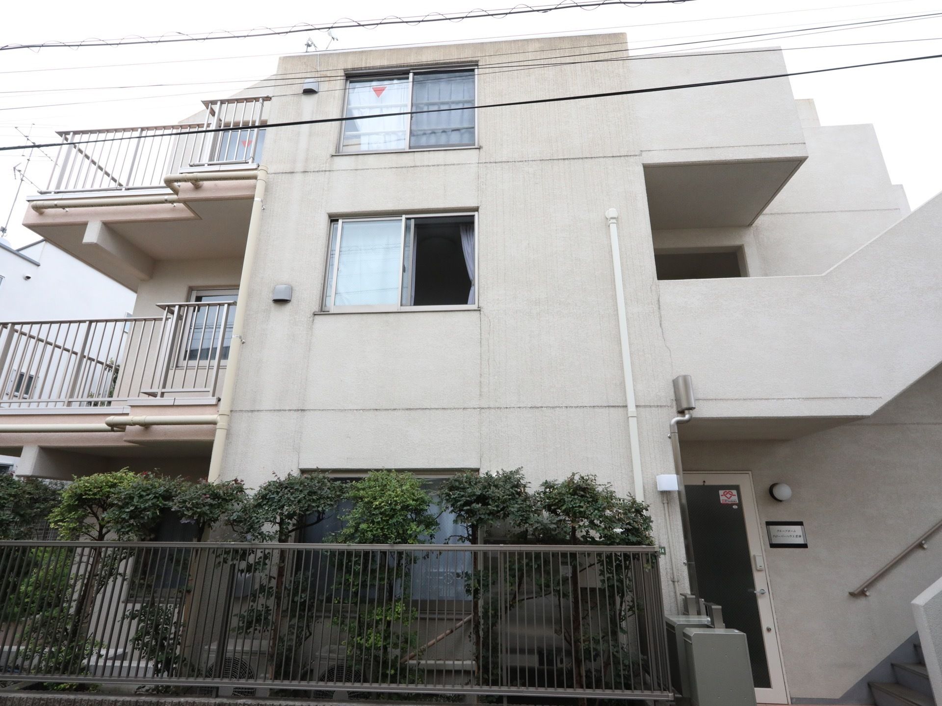 白いコンクリート造りの建物で、側面部分には窓が多く取り付けられている。柵の内側には樹木が植えられている。
