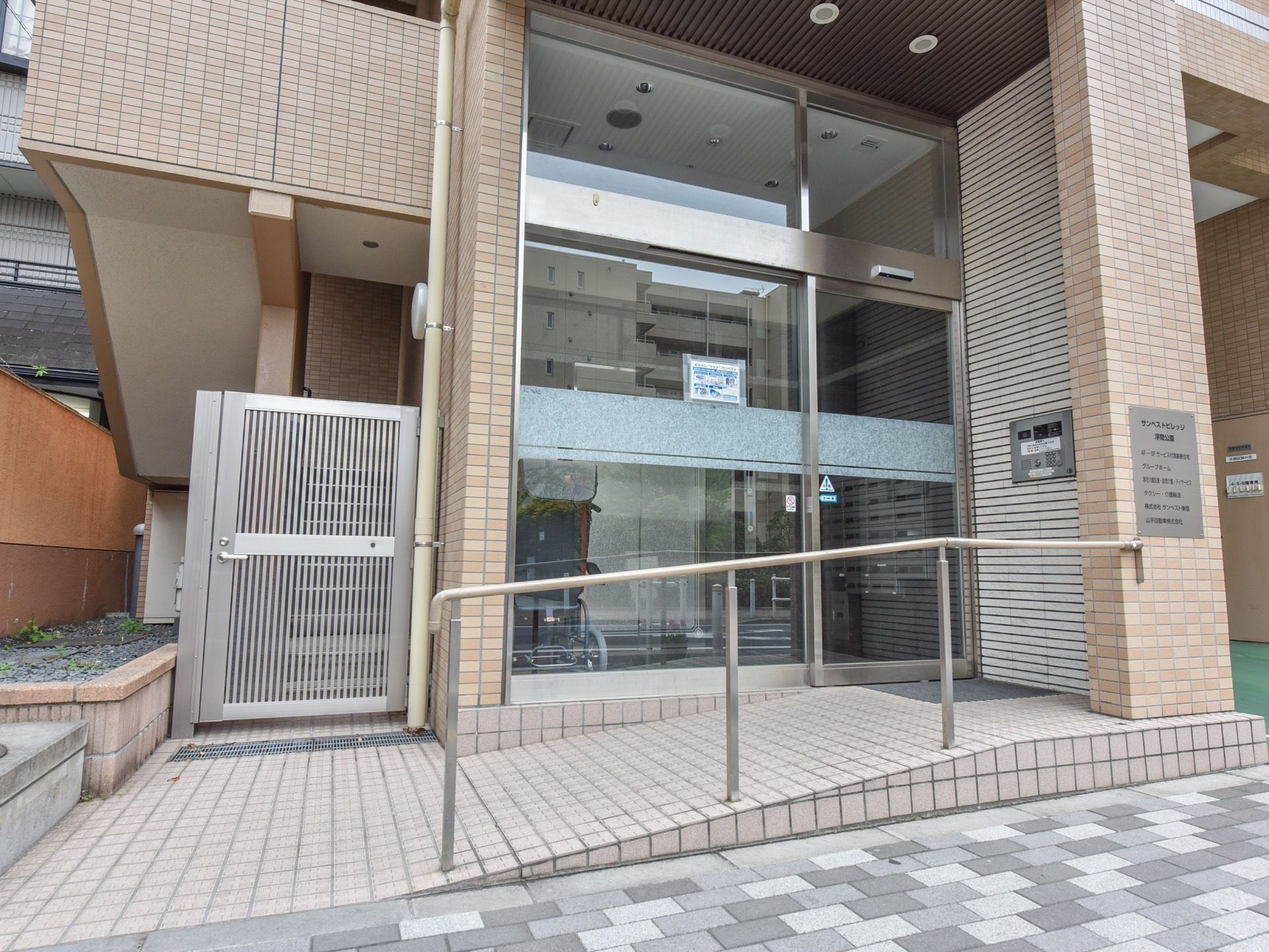 自動扉の玄関である。道路から玄関へは、スロープと手すりが完備されている。横には非常階段への扉が設置されている。
