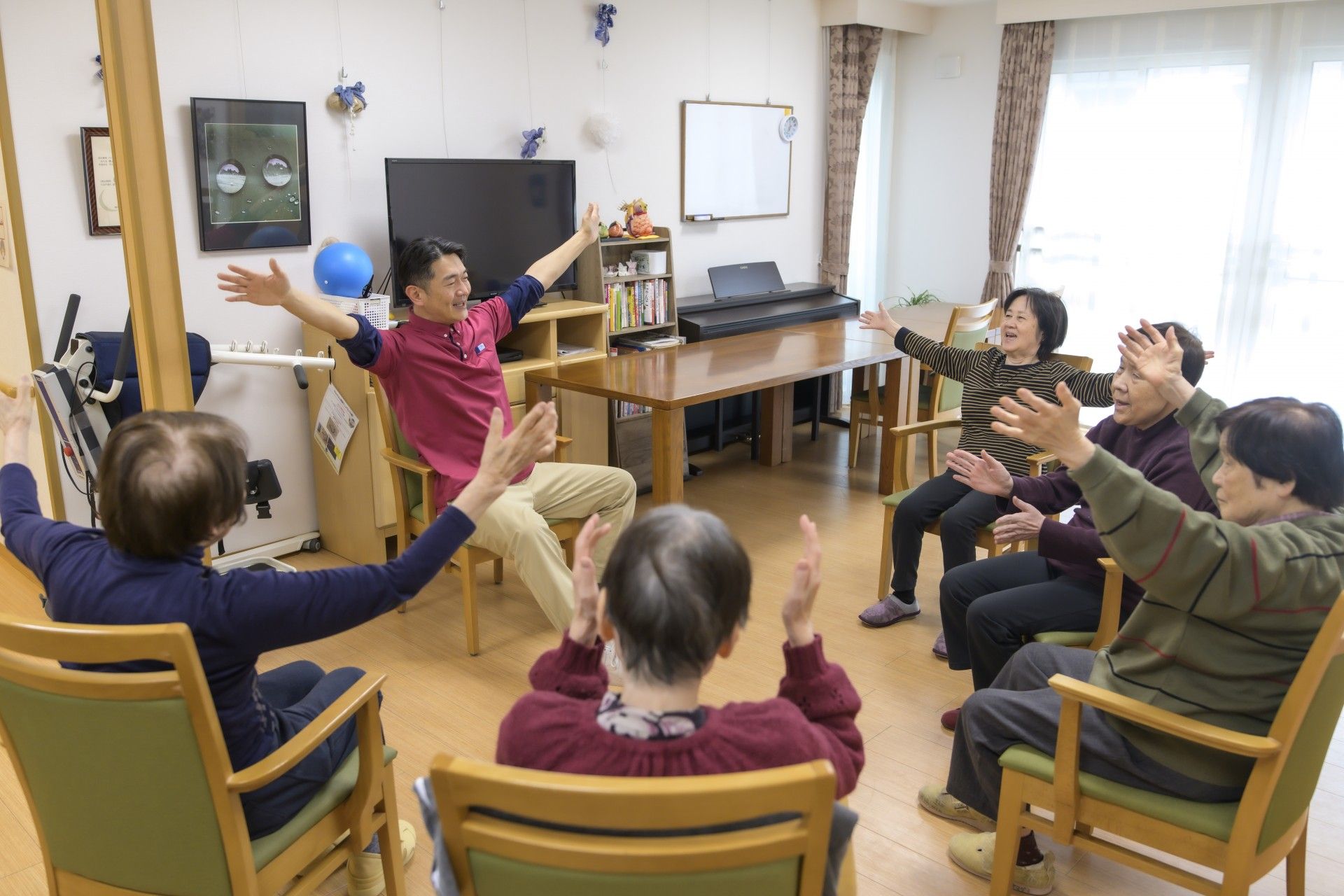 自然が広がる場所で車いすに乗りリラックスする女性とスタッフ。カメラに笑顔を向けている様子