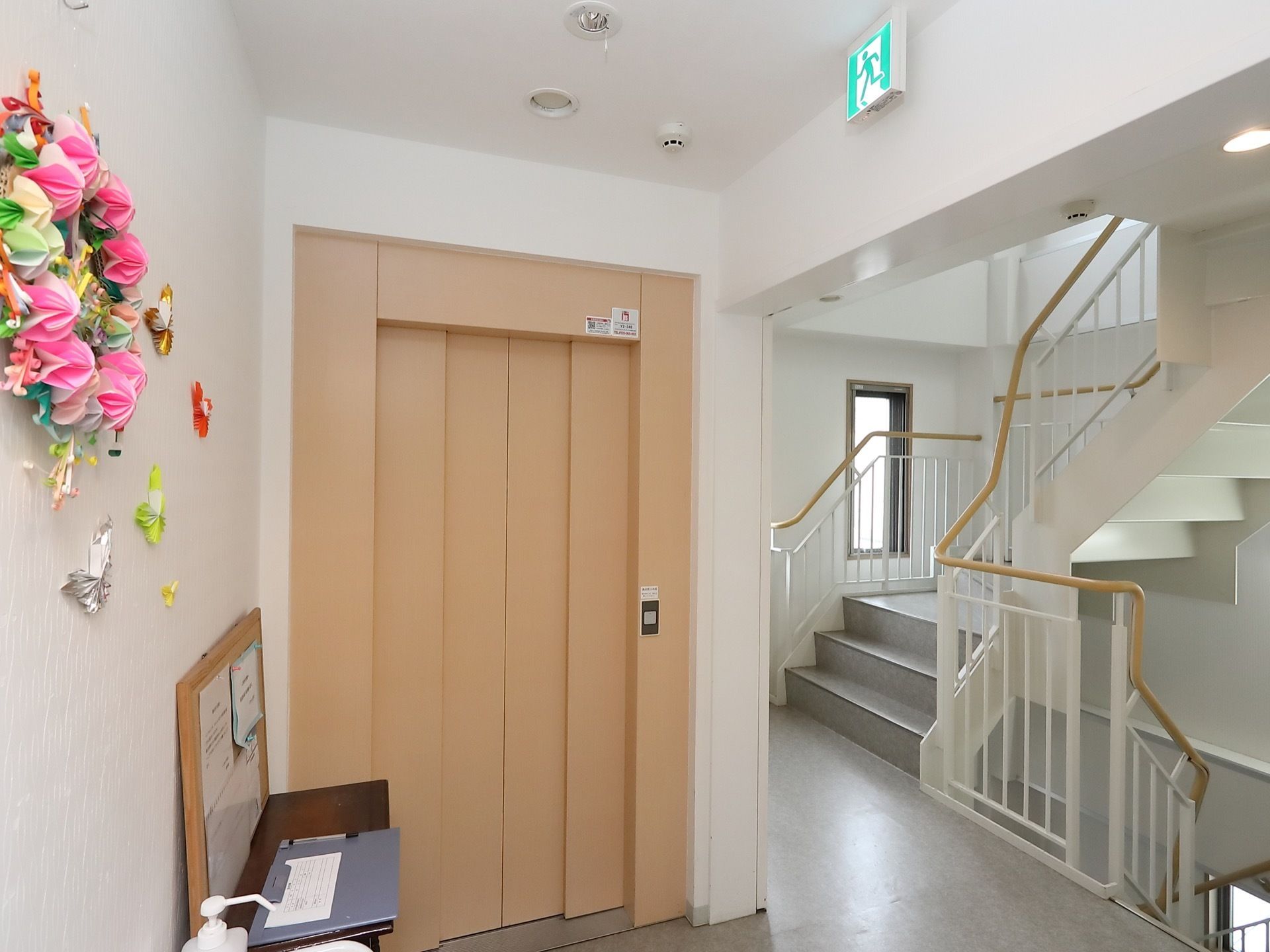 右手置くにはらせん状の階段があり、上下の階に続いている。正面にエレベーターがあり、ベージュの扉が閉まっている。