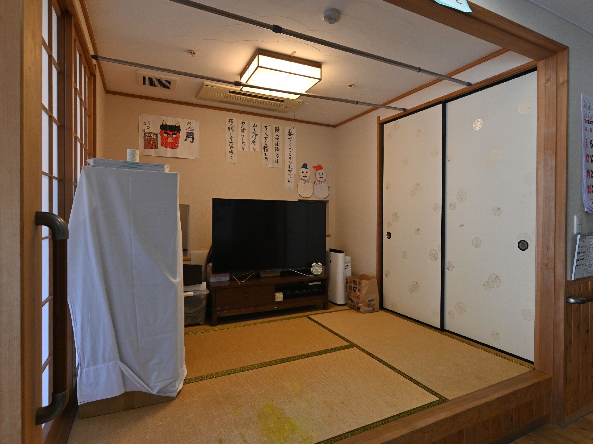 青いユニフォームを着た男性スタッフと高齢女性が笑顔で体操をしている。