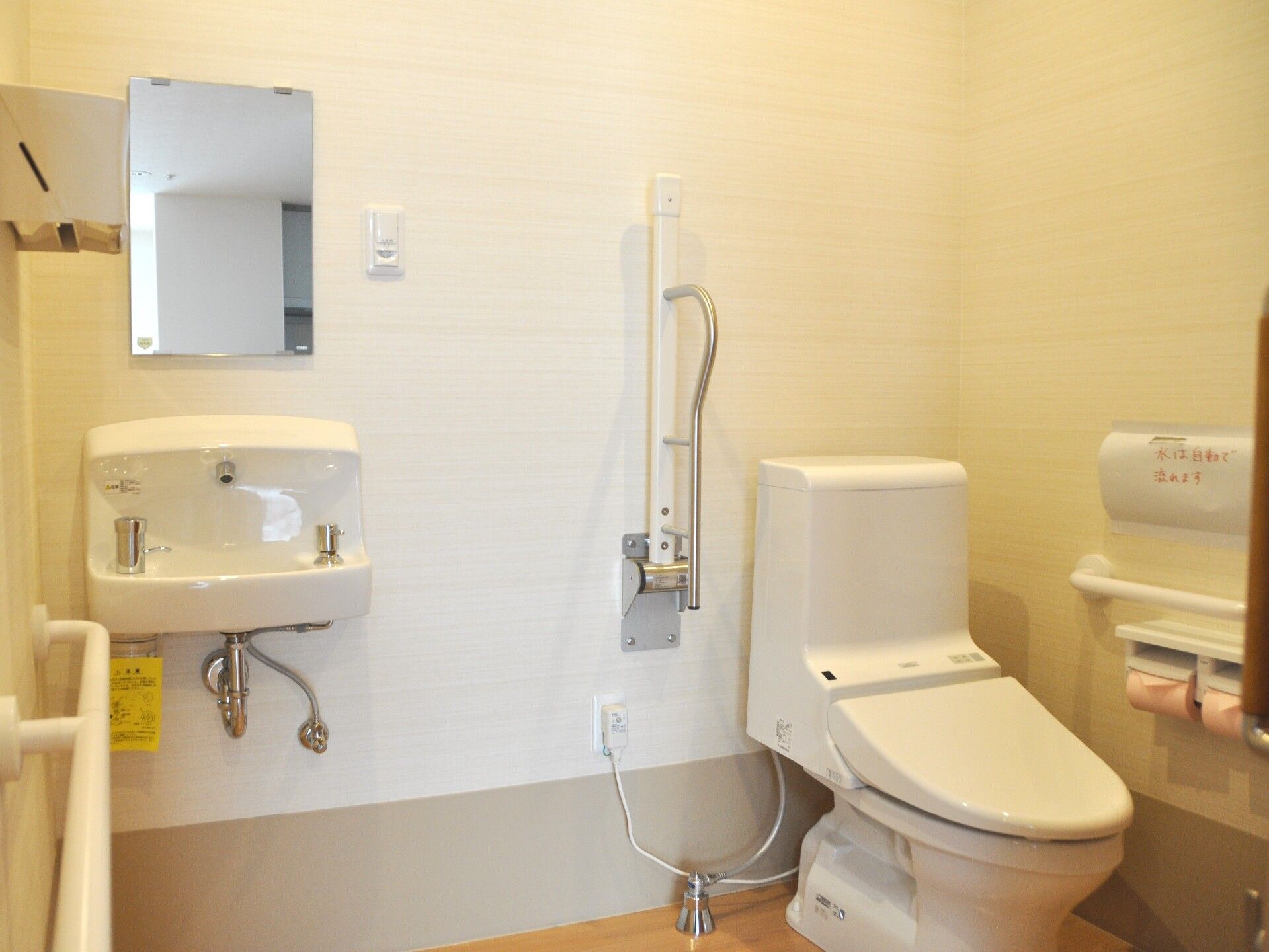 小さな洗面台がついている施設内のトイレの様子。手すりが取り付けられているトイレ