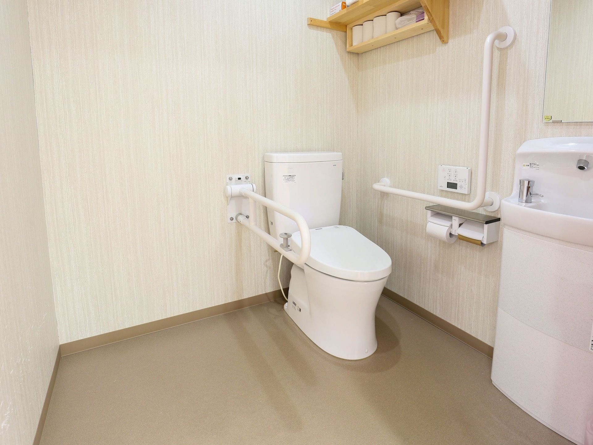 個室トイレの図である。床はダークブラウンのフローリングで、白い壁で囲まれている。中央にふたが閉められた便座がある。