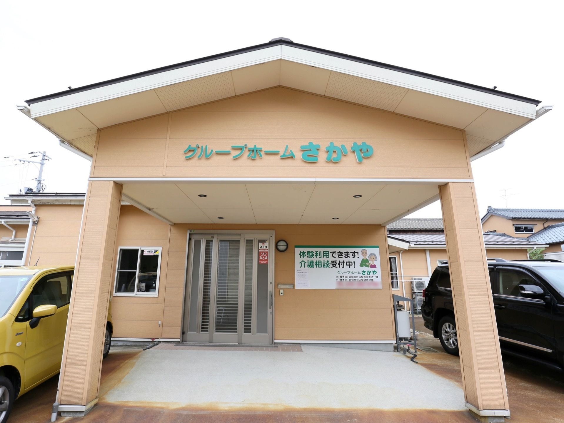 三角屋根付きのポーチが完備されている施設入口である。正面には、施設名称が文字プレートで設置されている。
