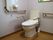 床はフローリングで、白い壁に囲まれた個室トイレである。中央に洋式便座があり、壁や便座周囲に手すりが用意されている。