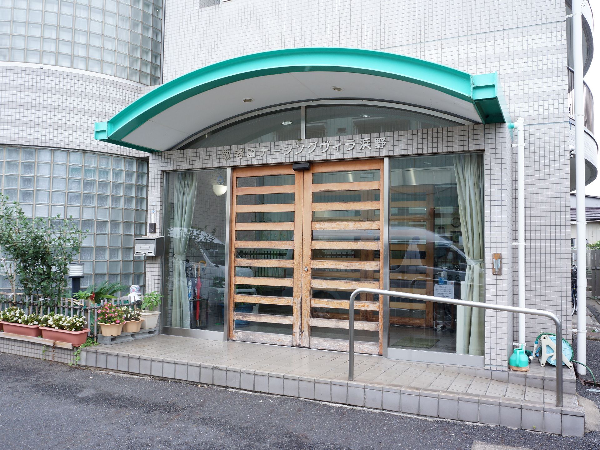 施設の玄関ドアは木製の枠にガラスがはめ込まれている。両脇はガラス張りである。上部にはシルバーの文字で施設名が書かれいる。