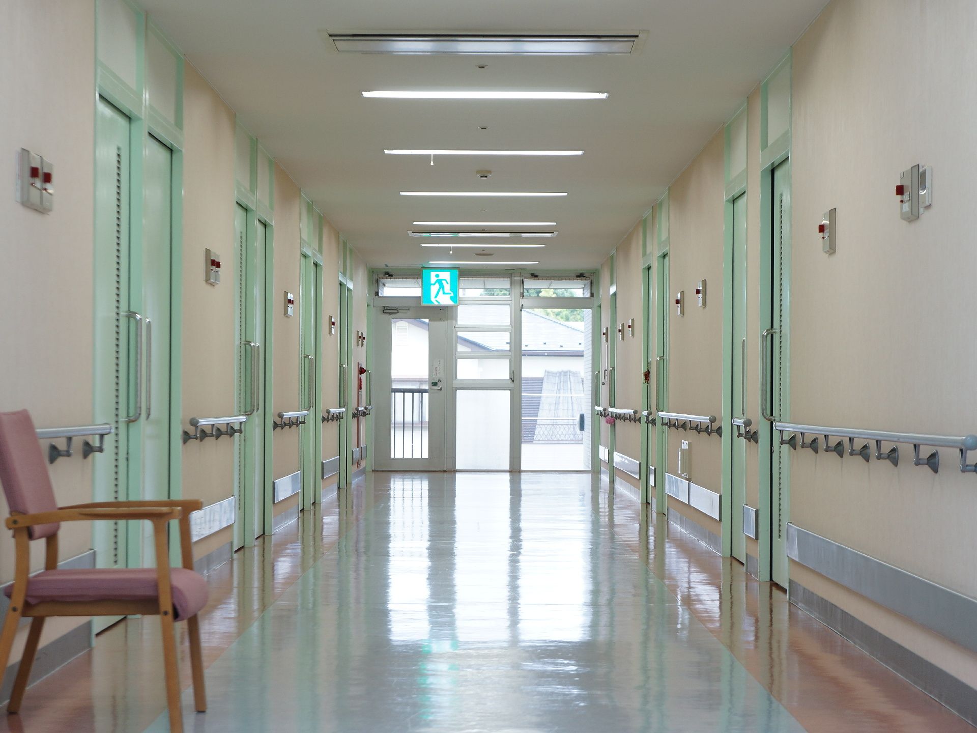 廊下の両側に手すりが取り付けられている。一人掛けの椅子が置かれている。奥は緊急避難経路になっている。