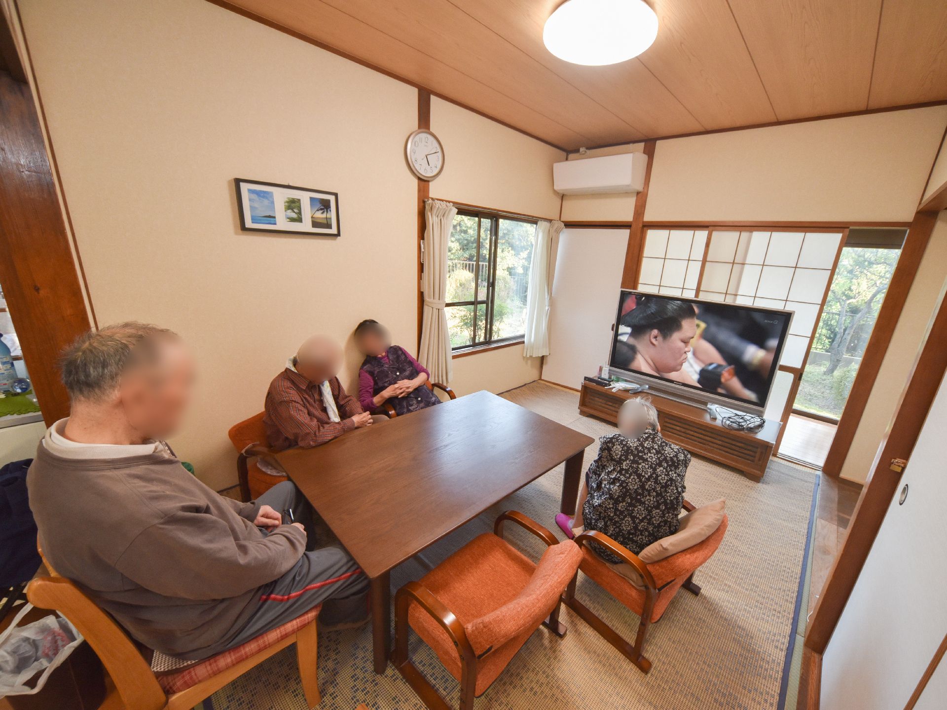 居間には大きなテレビが置かれ、現在は入居者様たちが相撲中継を見ている。障子のある窓からは緑の庭が見える。