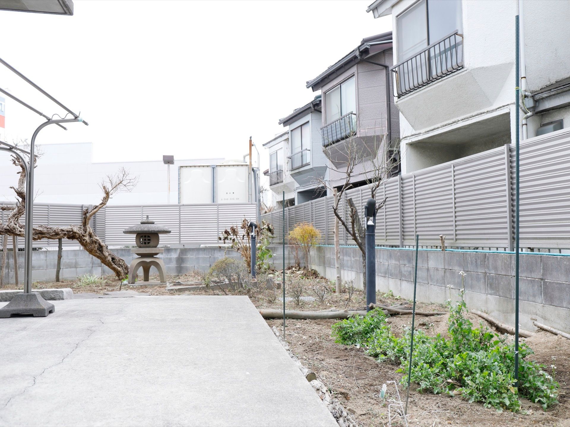 左側の地面はコンクリートで固められている。その上に物干し竿が設置されている。庭の周囲はフェンスで囲まれている。