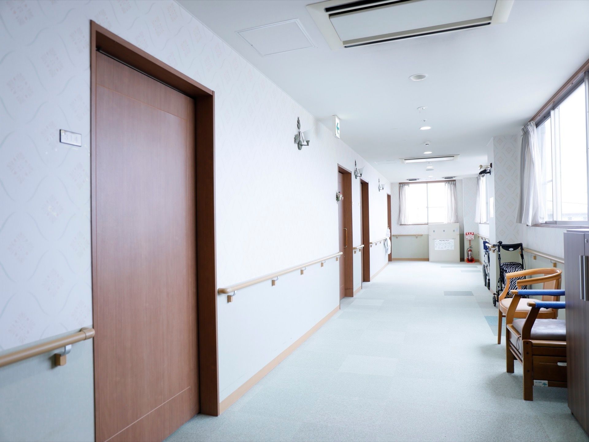 廊下には窓が数多くあるので、日中は光がよく当たり、明るい。壁沿いには手すりが設置され、休憩用の椅子も設置されている。