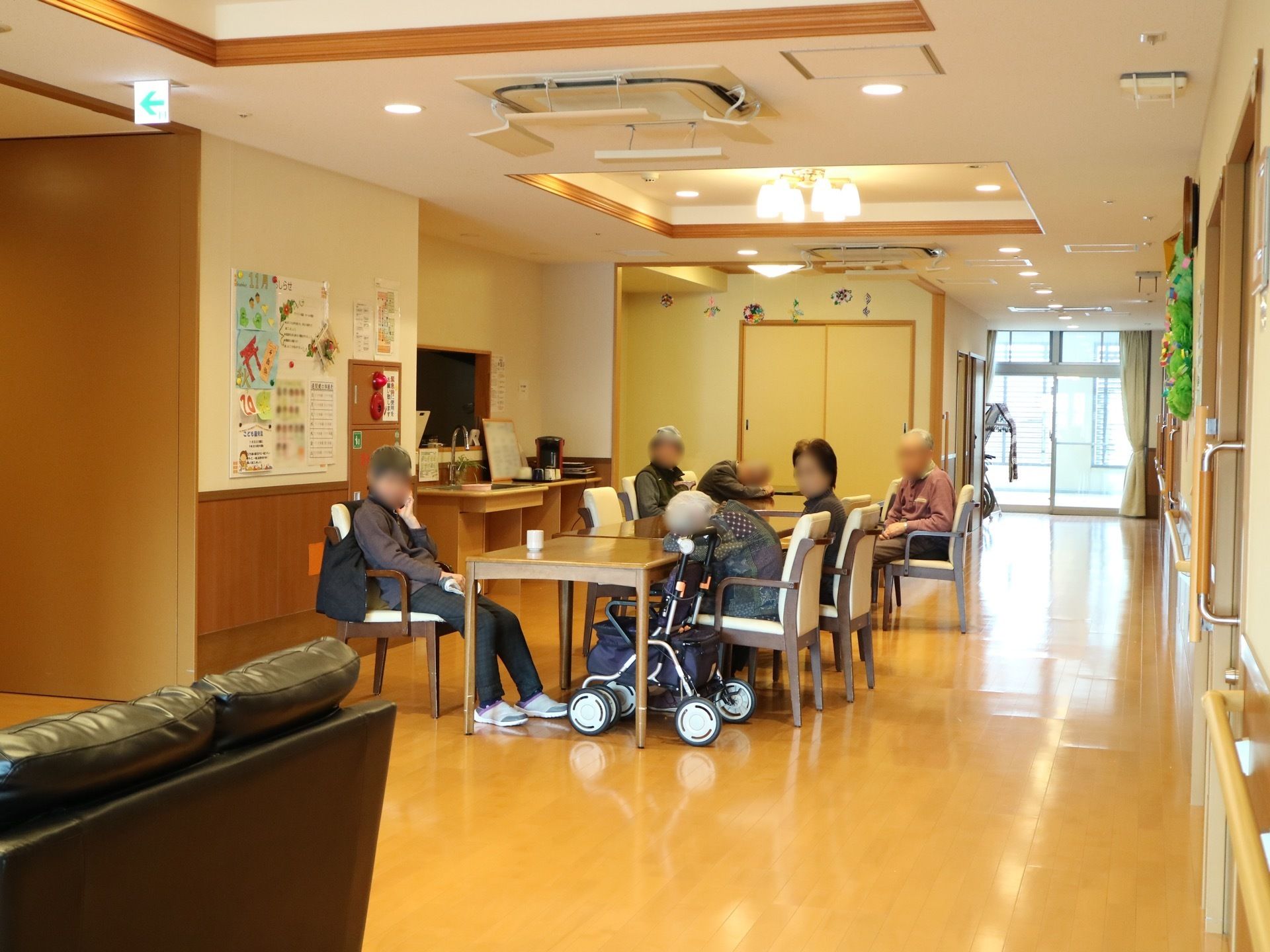 奥まで共有スペースが続いている。突き当りは窓になっており、外光が差し込んでいる。中央のテーブルで入居者様がくつろいでいる。