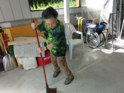 ほうきをもって掃除をしている女性入居者。奥には自転車などが置かれている。