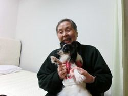白と黒の犬を抱えてベッド上で嬉しそうに笑う入居者の姿。