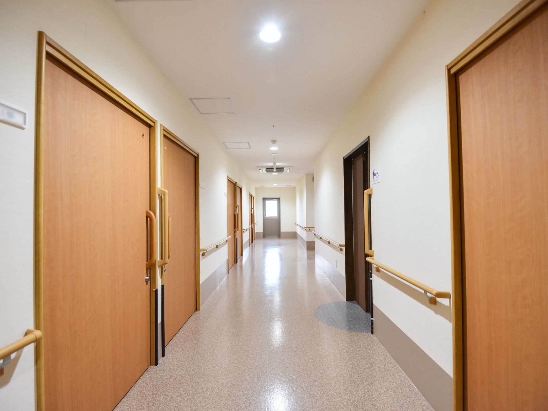 明るい通路を挟んで居室のスライドドアが並んでいる。両側の壁沿いに手すりを取り付けて、バリアフリー対策に取り組んでいる。