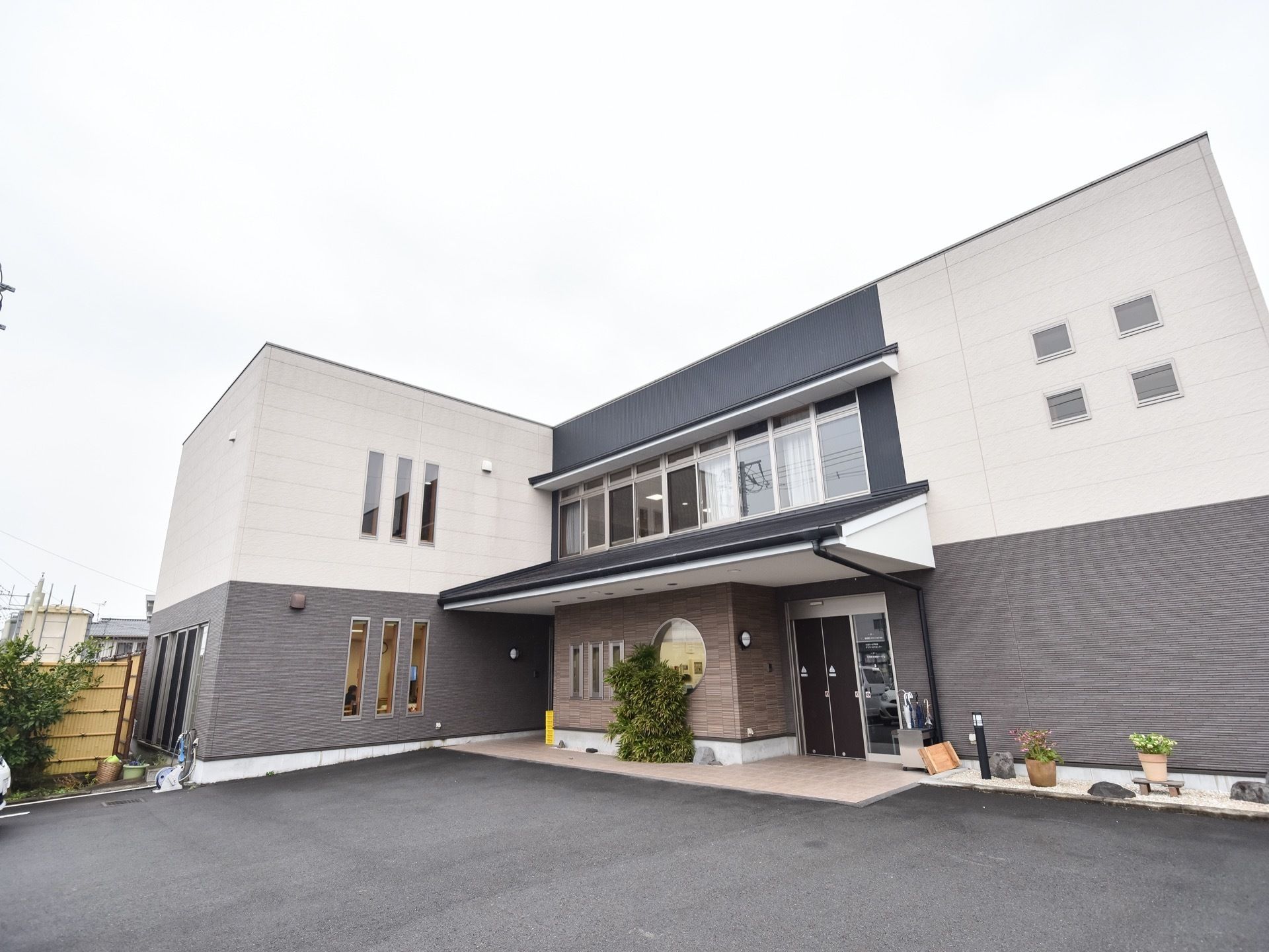 大きな窓があって日当たりの良い２階建て施設の外観である。建物の向かい側は、駐車スペースになっている。