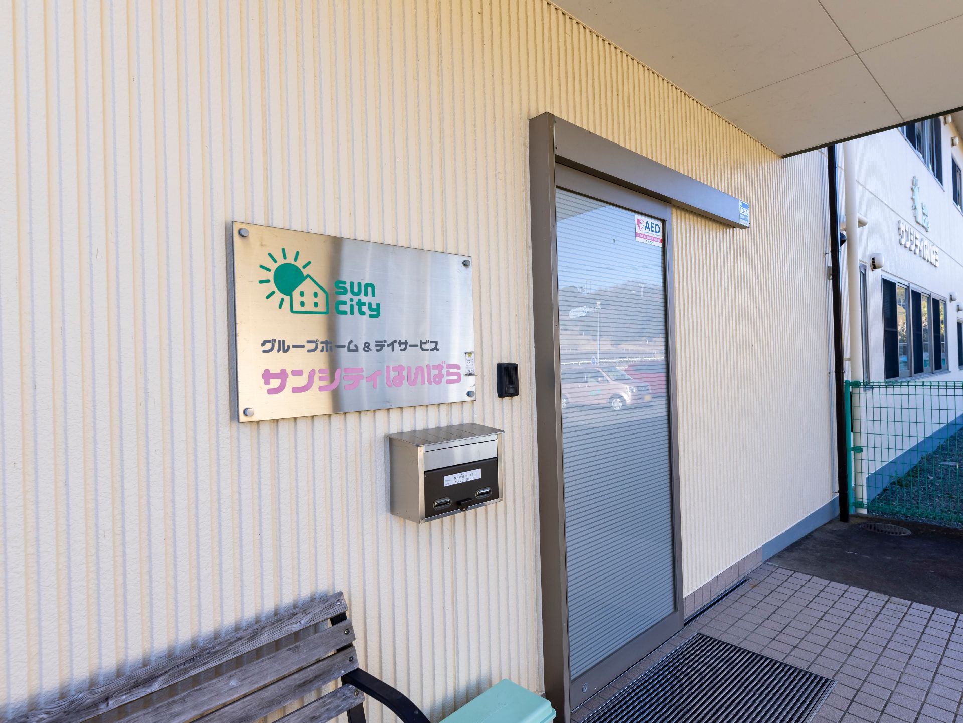 カーディガンを着た高齢女性とピンクのエプロンを付けた若い女性スタッフが寄り添い、笑っている。