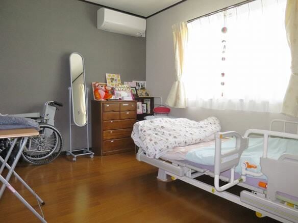 エアコンが付いたフローリングの部屋には寝具付きのベッドが置かれ、鏡やチェストなども置かれている。