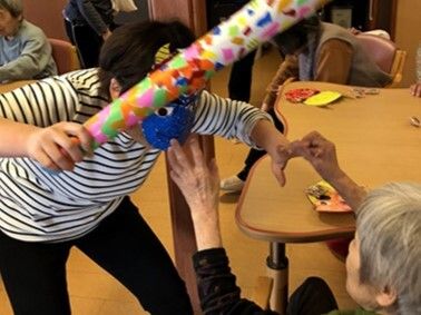 節分イベントの際の一コマ。鬼のお面ををかぶり、手作りのカラフルなかな棒を持ったスタッフと高齢女性。