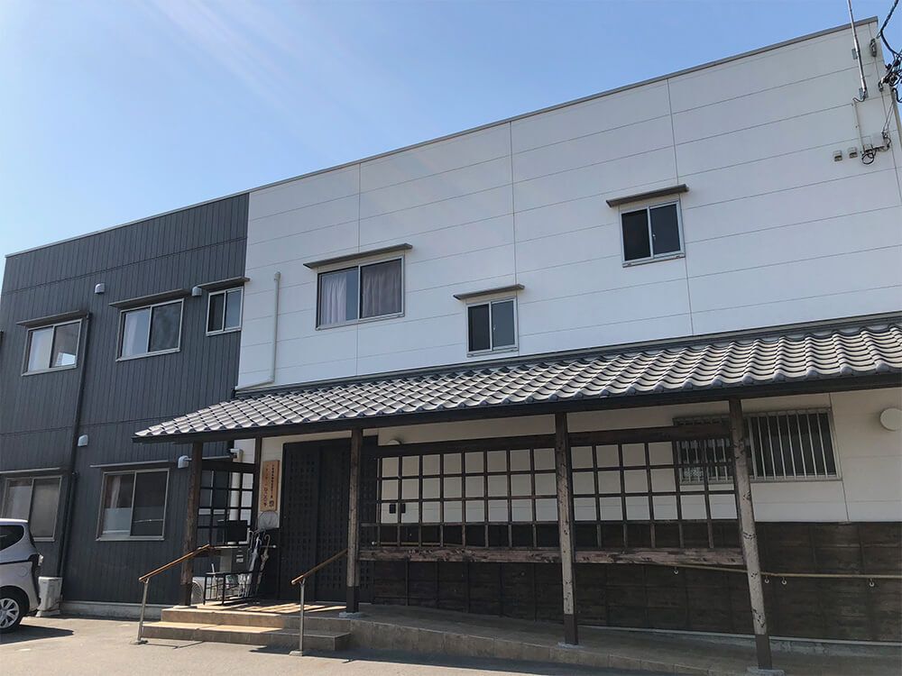 ２階建ての建物は日当たり良好で白とダークグレーの外壁で1階部分には瓦屋根が付いている。