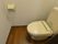 一人用のトイレの個室は、ダークブラウンのフローリングの床になっている。タンク付きのトイレとトイレットペーパー掛けが設置されている。