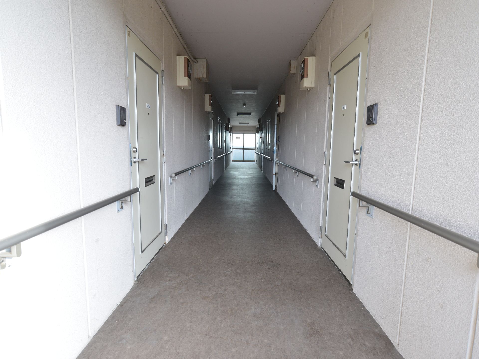 白を基調とした廊下には、居室の扉が多数並んでいる。壁には、同じ高さのところに手すりが取りつけられている。
