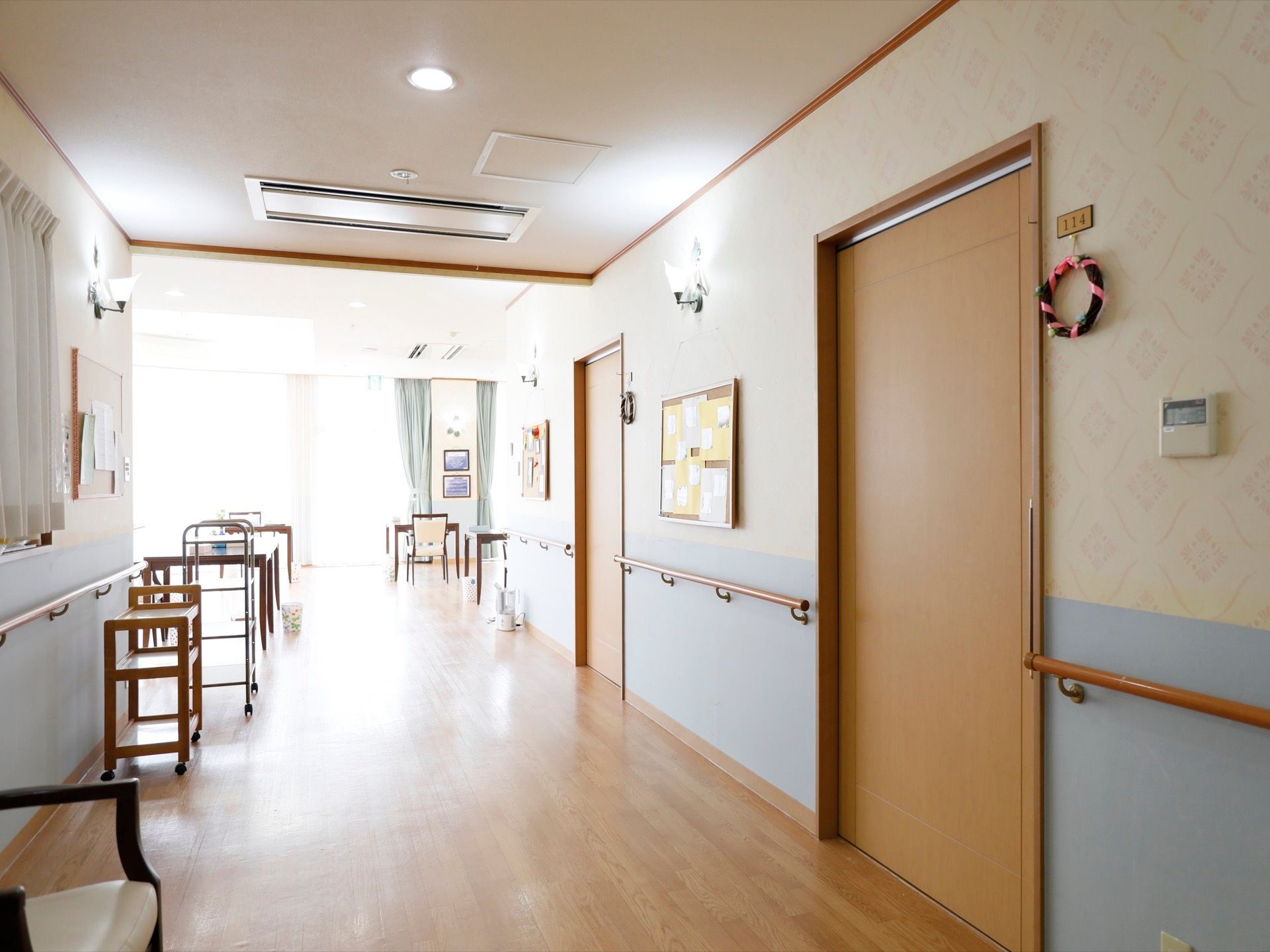 大きな掃き出し窓が奥にあり、太陽の光がサンサンと差し込んでいる。居室のドアが右側に並んでいて、すぐ横にリースが飾ってある。