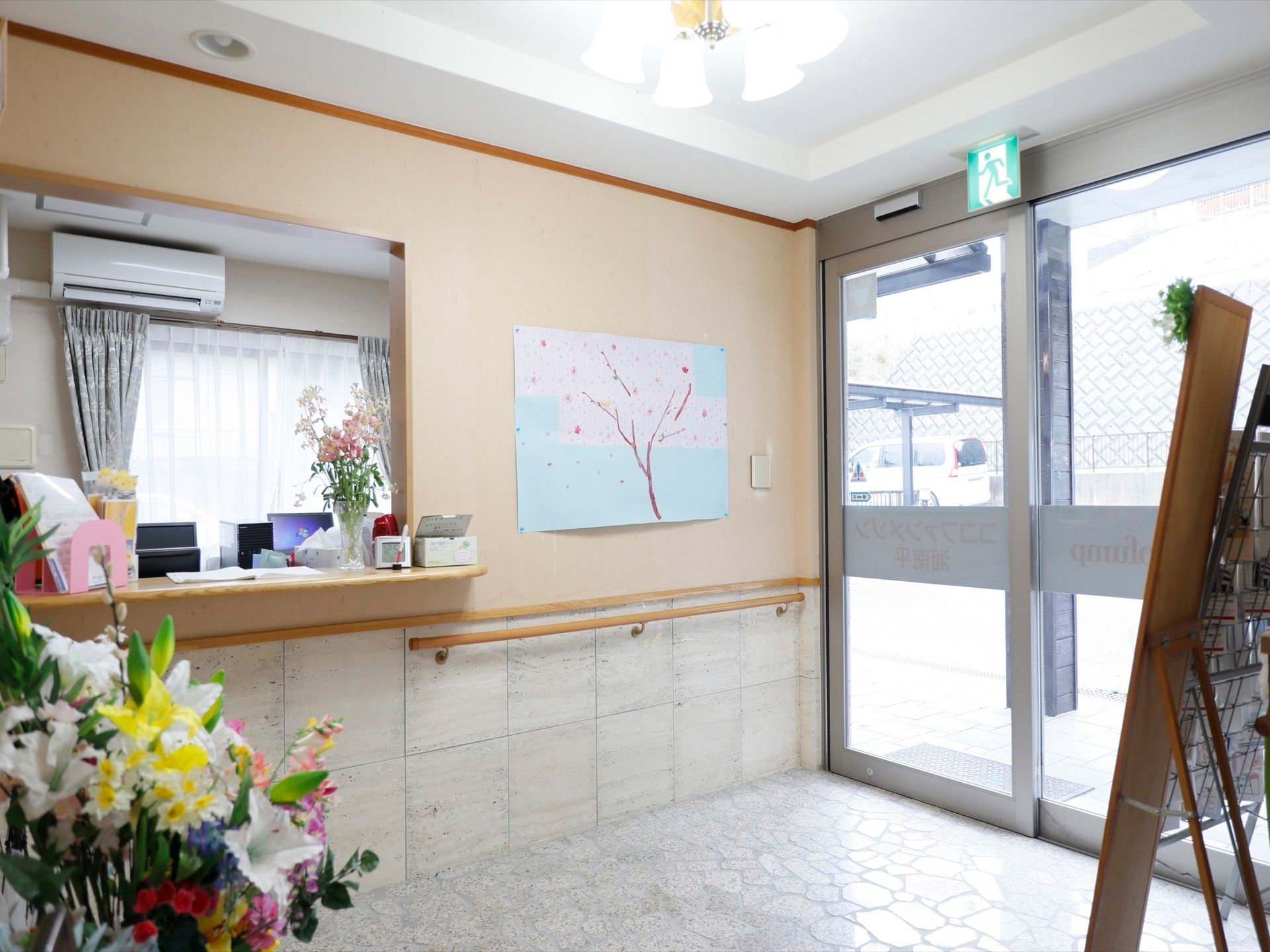 受付窓口の右横の壁には、サクラの花の絵が貼ってある。その下に、ベージュ色の長い手すりが取り付けられている。