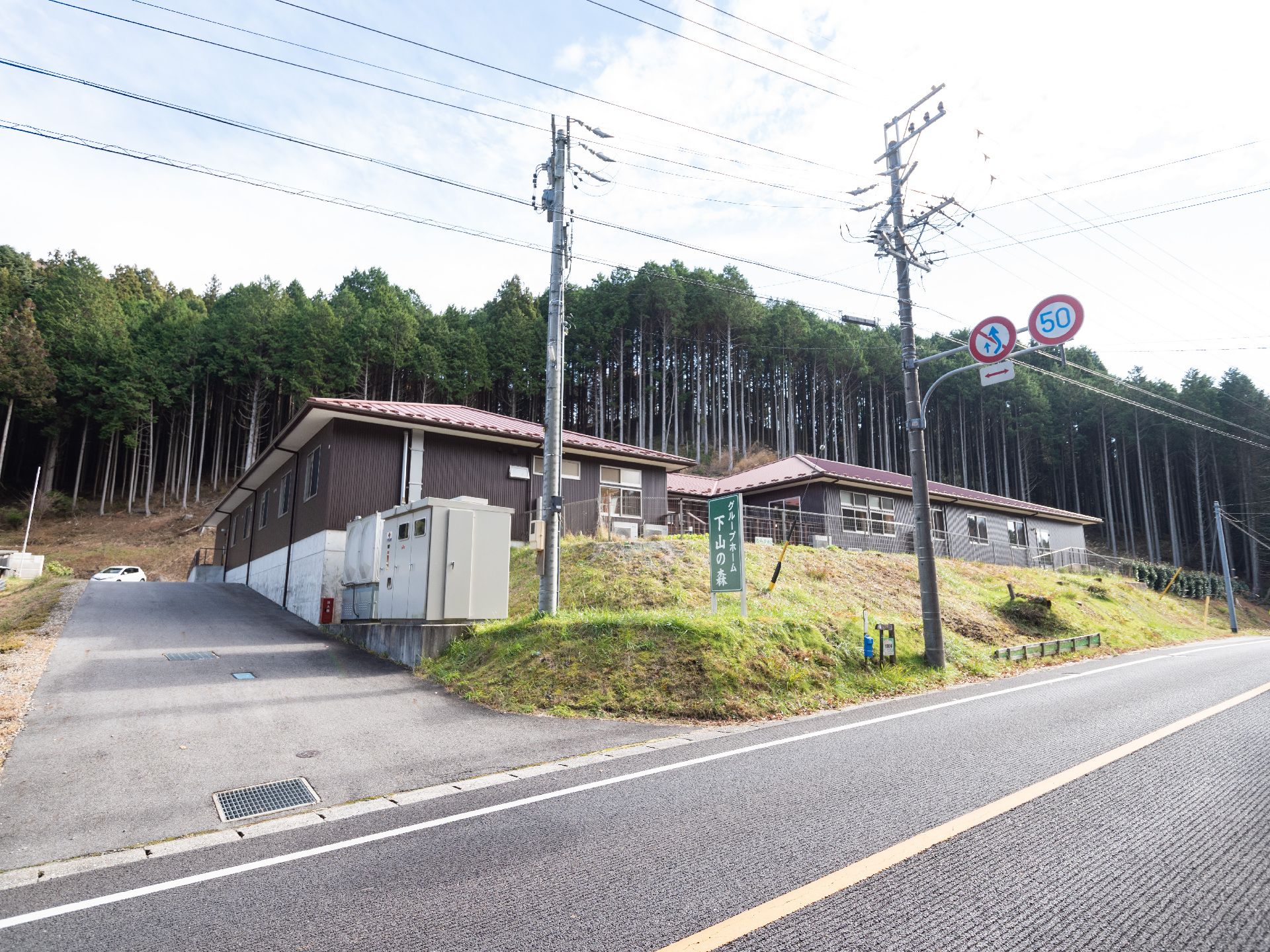 針葉樹林を背景に道路から小高い位置に立地する施設の外観