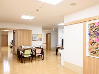 壁に飾られている掲示物が手前にあるリビング。奥のほうに家庭用のいすやテーブルが二つ並んでいる様子