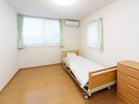 タンスが手前に写っている居室内の様子。介護仕様のベッドと窓、エアコンが写っている様子