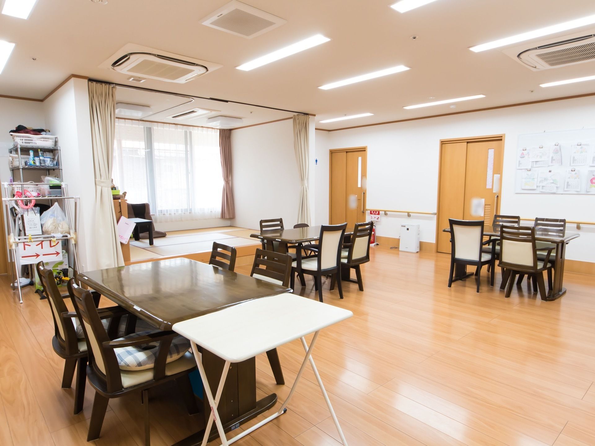 濃い茶色のテーブルと白い補助テーブルが置かれている。壁には手すりが取り付けられているほか、複数の掲示物がある。
