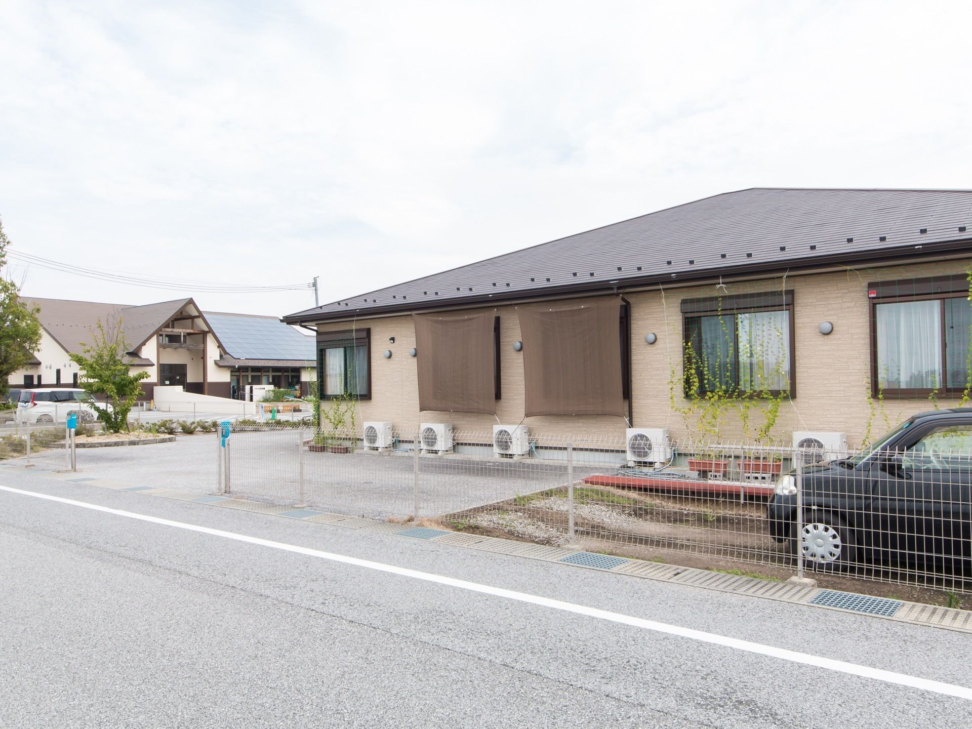 平屋建ての建物である。周囲は鉄製のフェンスで囲まれており、車が１台停まっている。また窓には、日よけのすだれがかかっている。