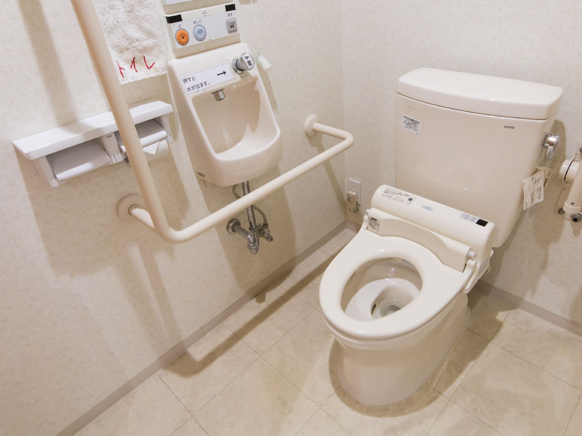 温水洗浄便座を完備し、壁に手すりや手洗い場が設置されたトイレ空間