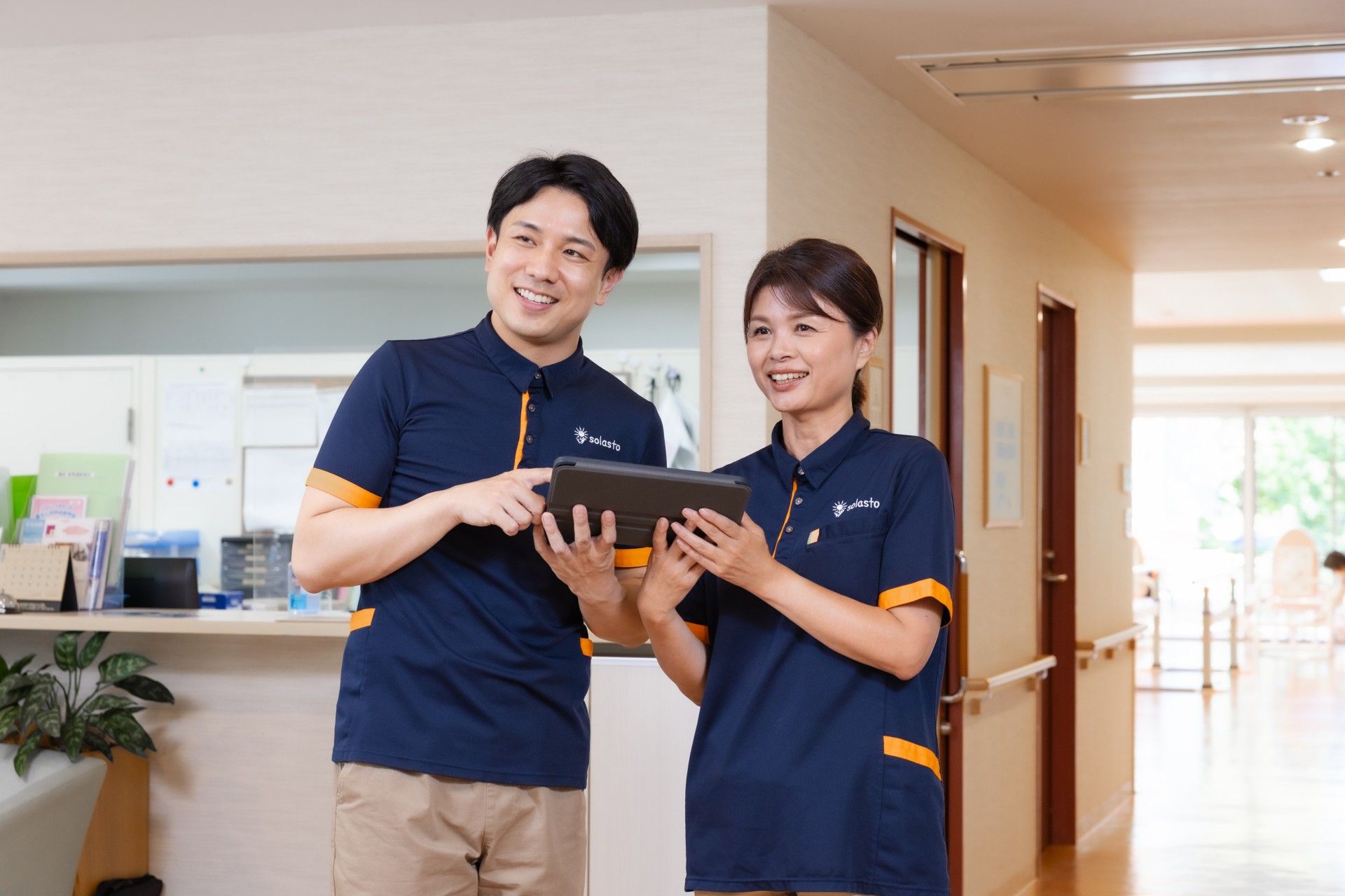 笑顔のスタッフがタブレットを操作する廊下