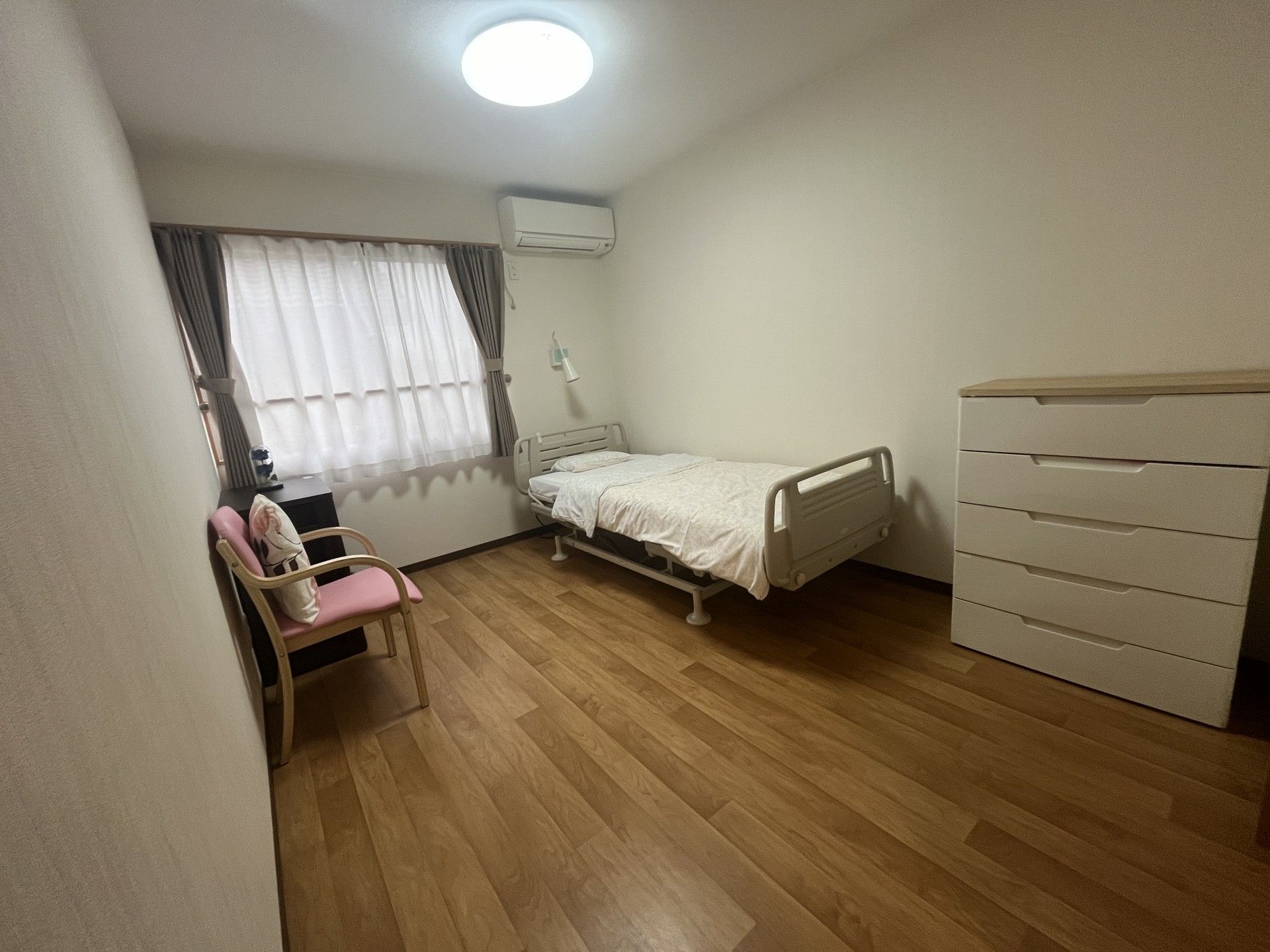 緑の多い屋外で散策を楽しんでいる車いすの高齢女性と付き添いのエプロンを付けた女性スタッフ。