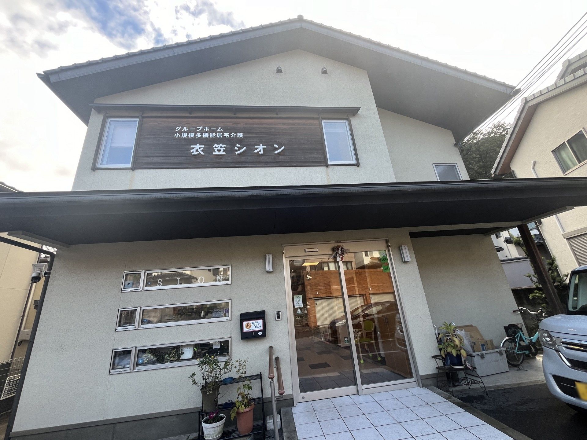 エプロンを付けた女性スタッフに手伝ってもらいながらフラワーアレンジメントを楽しんでいる高齢男性。