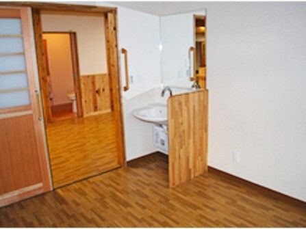 洗面所が付いたフローリングの部屋には和風の引き戸が設置され、家具は置かれていない。廊下の向こう側にはトイレがある。