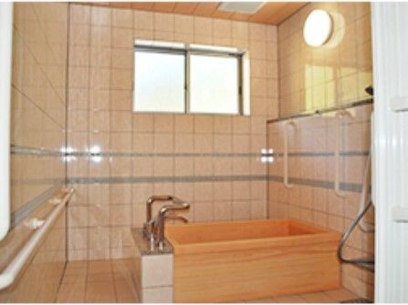 木製の一人用の浴槽が設置されたタイル張りの浴室にはたくさんの手すりが付き、シャワーもある。