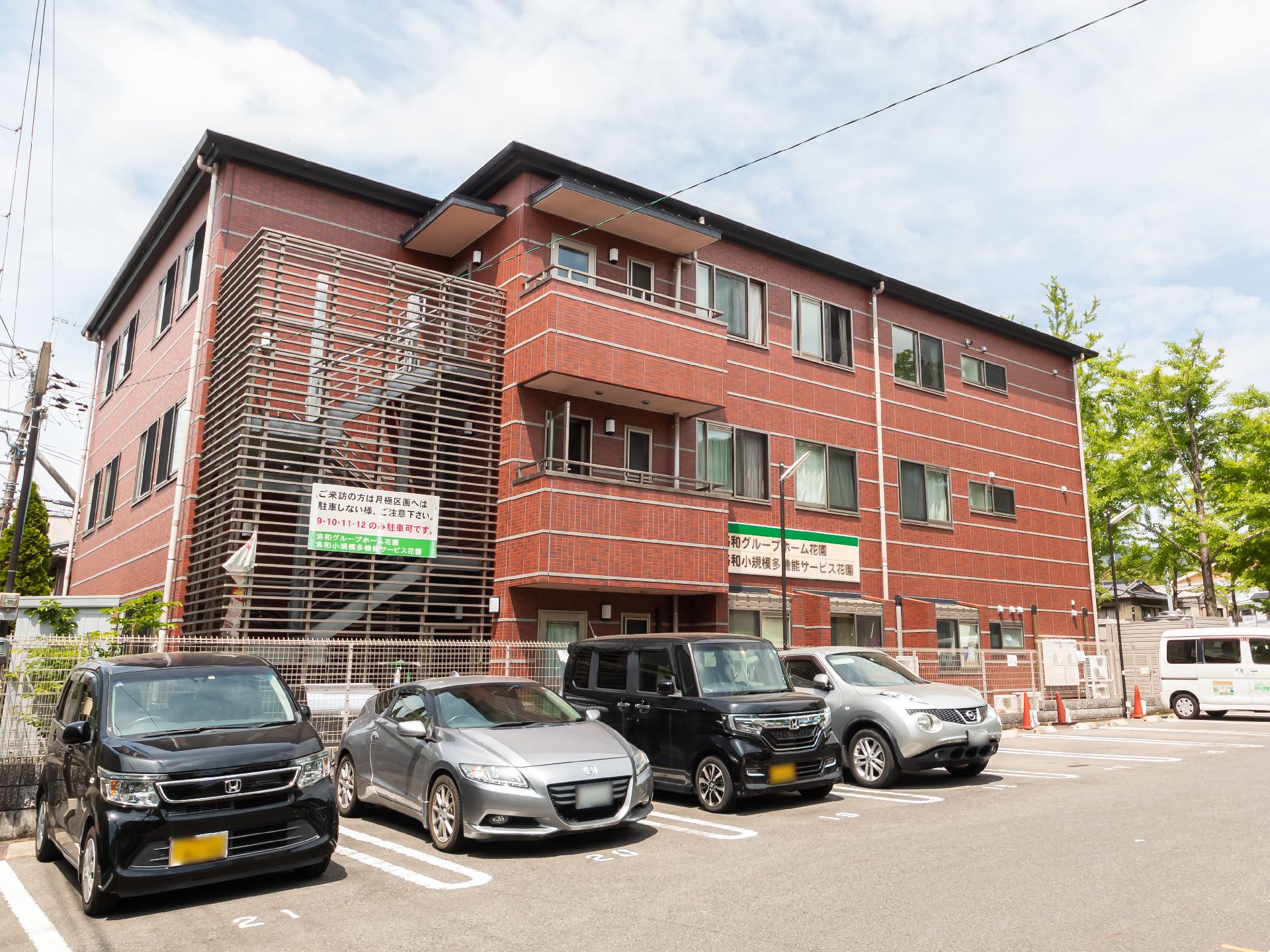 ブラウン系の３階建ての建物は明るい雰囲気で、そばには掲示板が設置されている。ホーム名が書かれた看板も電信柱に設置されている。