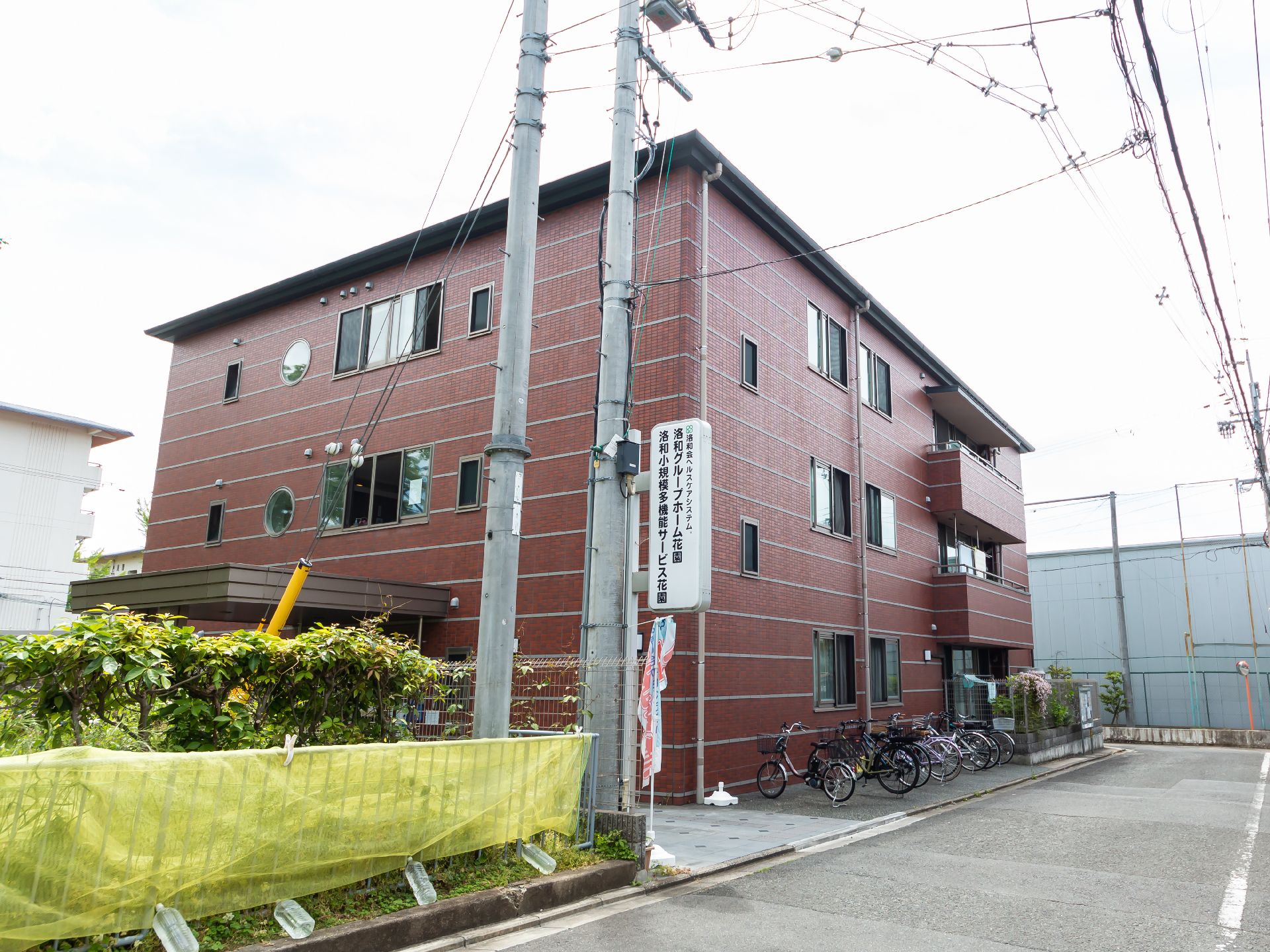 3階建ての建物のブラウン系で、建物のそばにある電信柱にはホーム名が書かれた看板もつけられている。