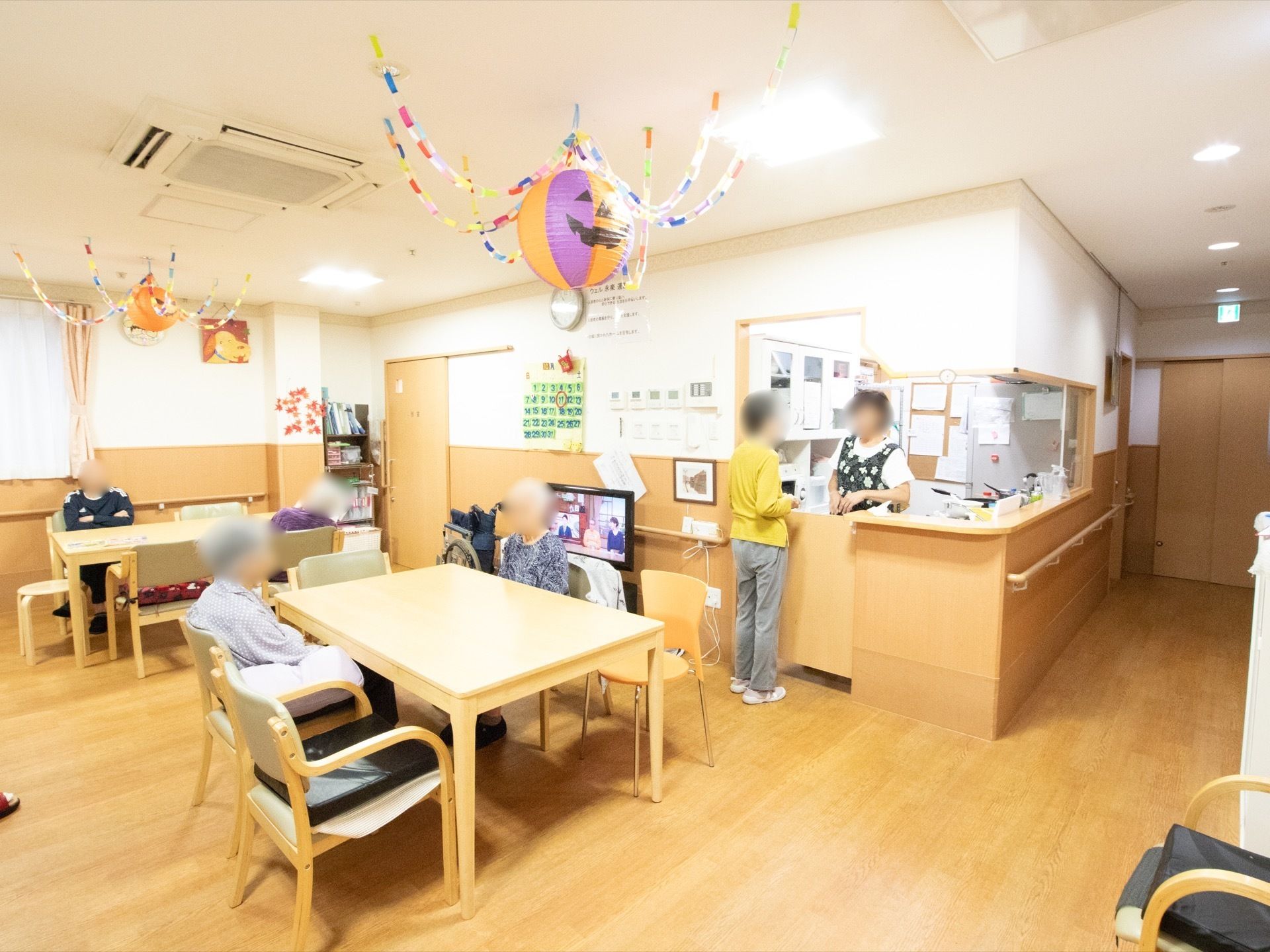 天井に埋め込み式のエアコンが設置されている。壁にはカレンダーや絵が飾られ、天井には季節の飾りもある。