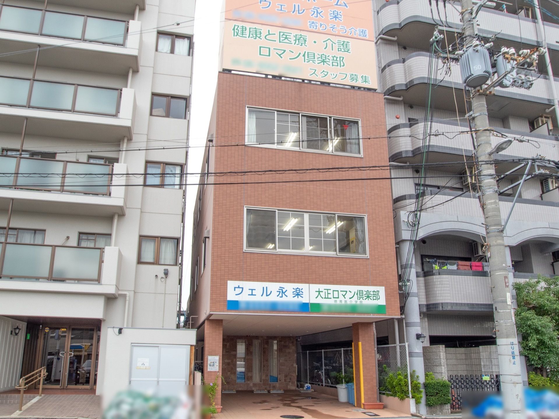 施設の建物は、１階が屋内駐車場になっている３階建てボックス型ビルのような外観である。ピンク系の外壁には施設名が大きく掲示されている。
