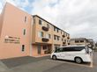 ベージュのタイルの壁に覆われている３階建ての建物がある。側面には大きく施設名が書かれており、建物の前面には駐車場がある。