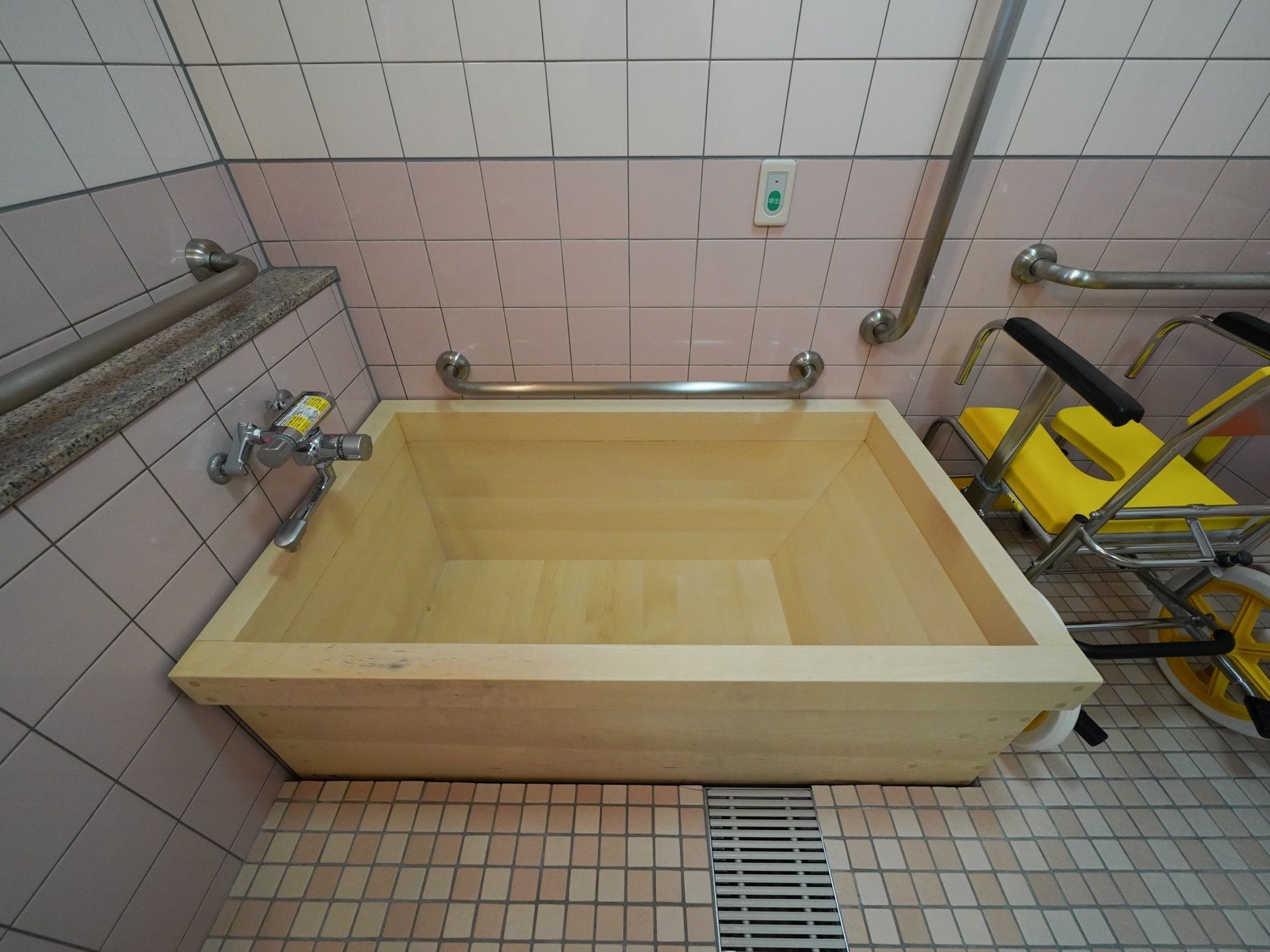 木製の浴槽になっている。壁には手すりと緊急時のナースコールが設置されており、入浴用車椅子も用意されている。